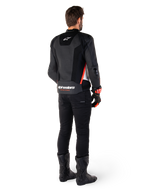 Motocyklista widziany od tyłu w skórzanej kurtce Alpinestars Missile V3 Airflow w kolorze Black White Red Fluo, w zestawieniu z czarnymi spodniami i butami, z obszerną perforacją skóry dla wentylacji, ochraniaczami ramion DFS i wyraźnym logo Alpinestars na dolnej części pleców.