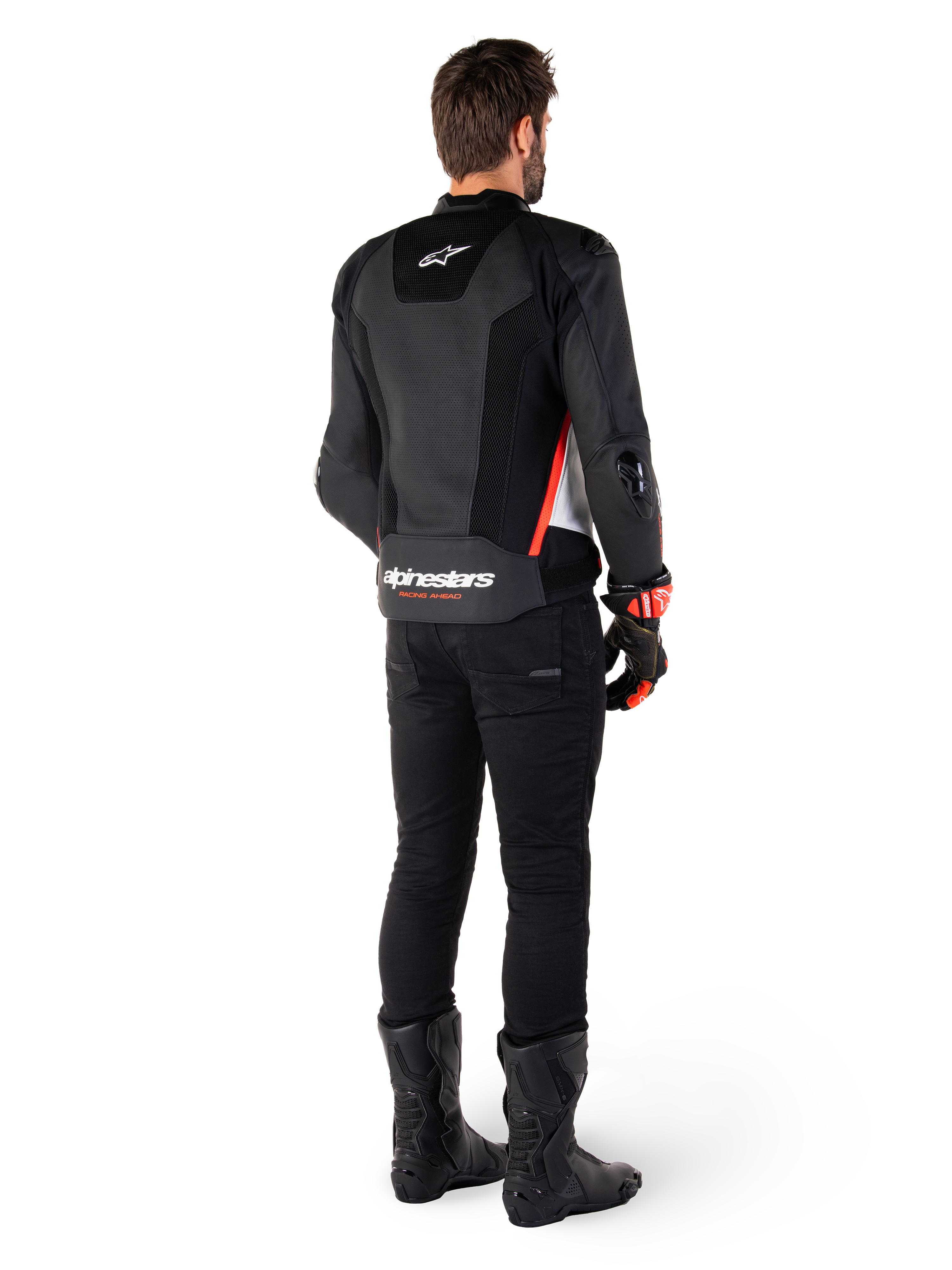 Motocyklista widziany od tyłu w skórzanej kurtce Alpinestars Missile V3 Airflow w kolorze Black White Red Fluo, w zestawieniu z czarnymi spodniami i butami, z obszerną perforacją skóry dla wentylacji, ochraniaczami ramion DFS i wyraźnym logo Alpinestars na dolnej części pleców.
