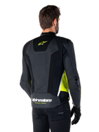 Skórzana kurtka Alpinestars Missile V3 Airflow, widok z tyłu na modelu, czarna z neonowożółtymi i białymi akcentami, posiada obszerne panele z perforowanej skóry i siatki na plecach, żółte logo gwiazdy oraz biały napis „RACING AHEAD”, zestawiona z czarnymi rękawicami i spodniami.