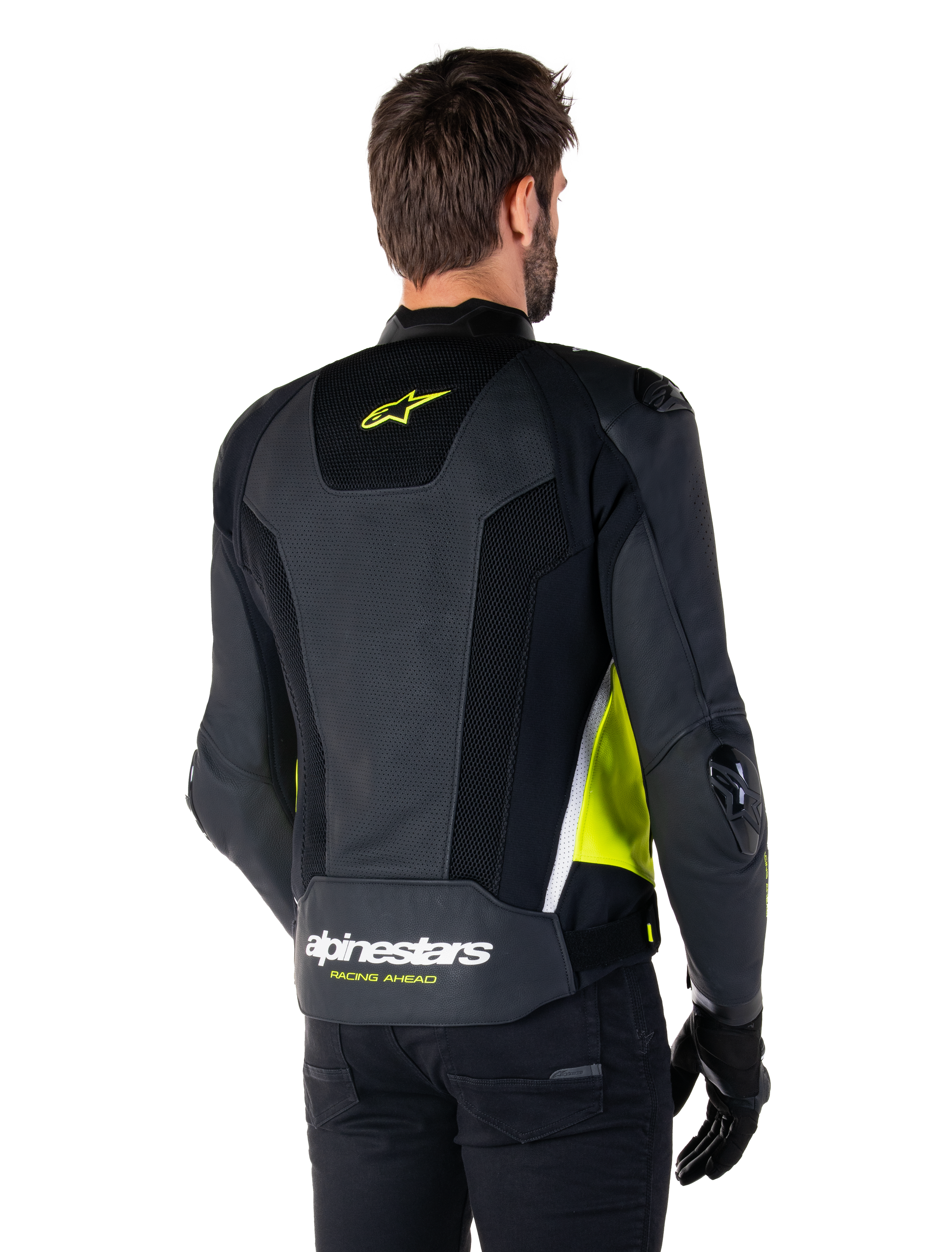 Skórzana kurtka Alpinestars Missile V3 Airflow, widok z tyłu na modelu, czarna z neonowożółtymi i białymi akcentami, posiada obszerne panele z perforowanej skóry i siatki na plecach, żółte logo gwiazdy oraz biały napis „RACING AHEAD”, zestawiona z czarnymi rękawicami i spodniami.