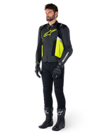 Model ubrany w skórzaną kurtkę Alpinestars Missile V3 Airflow w kolorze czarnym, żółtym fluo i białym, zestawioną z czarnymi rękawicami, spodniami i butami motocyklowymi, prezentujący perforowaną skórzaną konstrukcję i estetykę inspirowaną wyścigami.