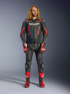 Męski model w skórzanej kurtce Alpinestars GP Force V2 w kolorze czarno-czerwonym Fluo, zestawionej z dopasowanymi skórzanymi spodniami, czerwonymi rękawicami wyścigowymi i czerwonymi butami sportowymi, profesjonalna odzież motocyklowa