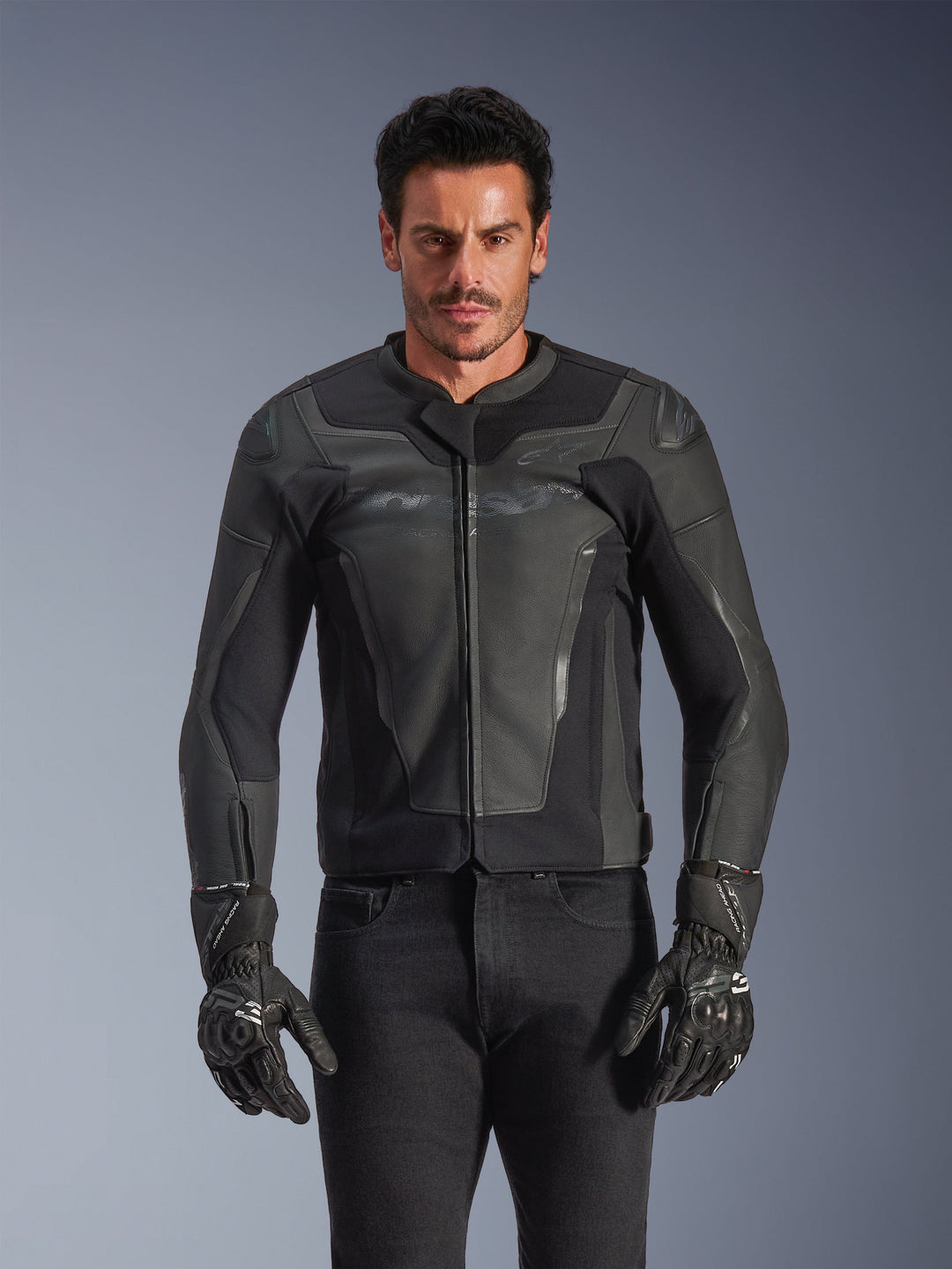 Skórzana kurtka Alpinestars GP Force V2, czarna i ciemnoszara, motocyklowa kurtka wyścigowa, mężczyzna w dopasowanym skórzanym fasonie z zamkiem z przodu, w połączeniu z czarnymi teksturowanymi rękawicami, nowoczesna odzież ochronna, konstrukcja ze skóry najwyższej jakości.