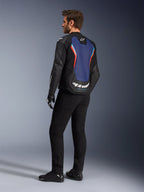 Widok z tyłu pod kątem trzech czwartych na modela ubranego w skórzaną kurtkę Alpinestars GP Force V2 w kolorystyce Black Blue Red Fluo, podkreślający niebieski panel na plecach z czerwonymi fluorescencyjnymi akcentami i białym logo, zestawiony z czarnymi spodniami i rękawicami motocyklowymi.