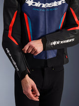 Alpinestars GP Force V2 Leather Jacket in Black, Blue, and Red Fluo, close-up view of a person adjusting the sleeve cuff zipper, featuring white Alpinestars logos on the forearm and chest, textured bovine leather construction for sport motorcycle riding