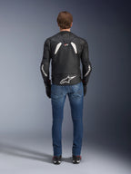 Widok z tyłu skórzanej kurtki Alpinestars GP Plus R V4 Rideknit, czarno-biała, z dużym białym logo w dolnej części pleców i brandingiem na rękawach, noszona z niebieskimi jeansami motocyklowymi i czarnymi butami, podkreślająca techniczną konstrukcję i sportowy krój.