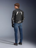 Alpinestars GP Plus R V4 Rideknit Leather Jacket, czarno-biała skórzana kurtka motocyklowa, widok z tyłu na modelu, biały branding Alpinestars na rękawach, duże logo gwiazdy w dolnej części pleców, niebieskie dżinsy, czarne buty motocyklowe, techniczna odzież motocyklowa