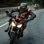 Motocyklista jadący na czerwonym motocyklu sportowym, skórzana kurtka Alpinestars GP Plus R V4 Rideknit, czarna z detalami w kolorze Red Fluo i białym, z białym logo Alpinestars i napisem „ASTARS”, w zestawie z czarnym kaskiem wyścigowym i rękawicami, wyczynowa odzież motocyklowa w akcji na drodze.