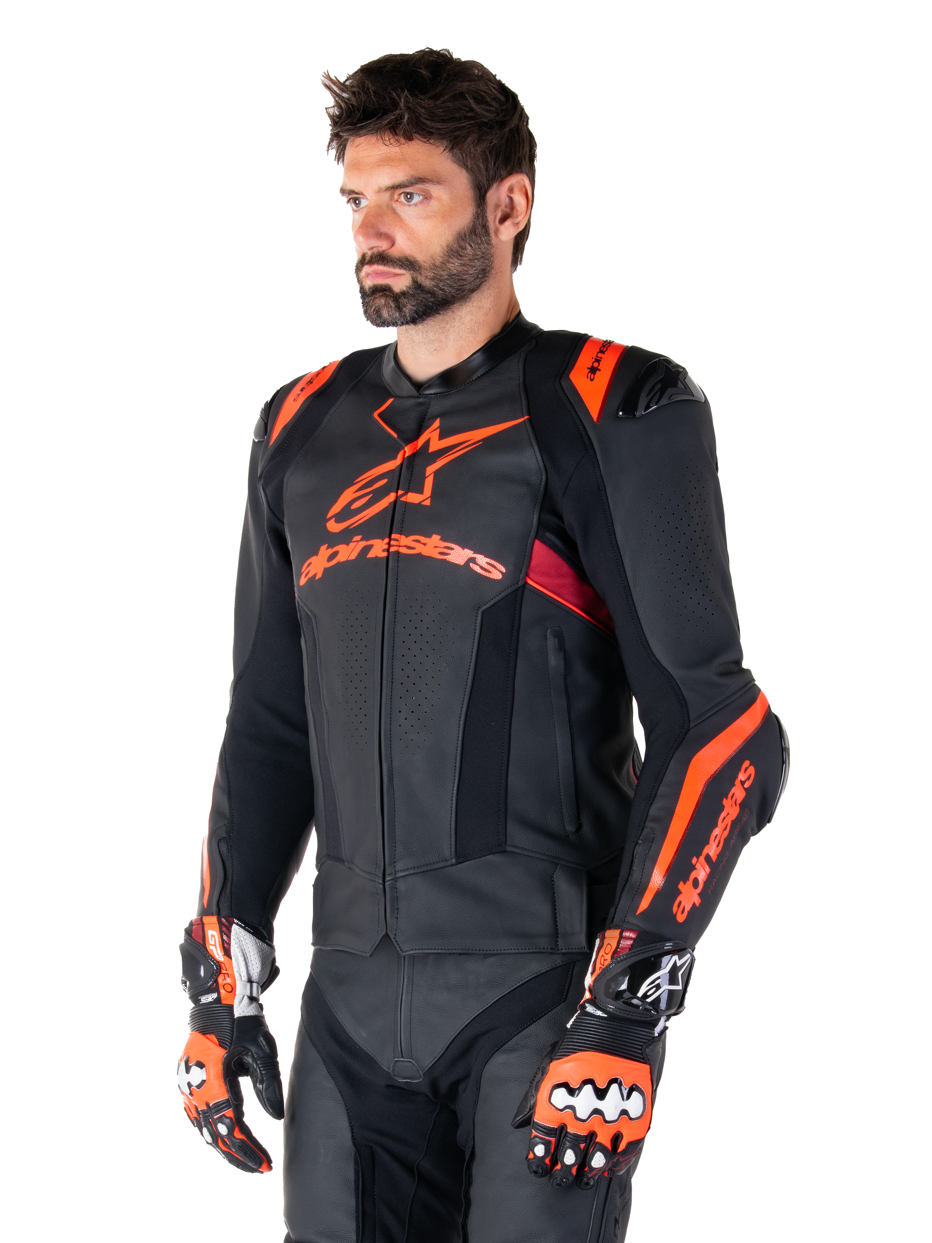 Alpinestars Missile V3 Ignition Leather Jacket, skórzana kurtka motocyklowa, czarna z akcentami w kolorze czerwonym fluo i ciemnoczerwonym, na modelu z pasującymi rękawicami wyścigowymi i skórzanymi spodniami, wyraźne logo Alpinestars, perforowane panele skórzane i zewnętrzne ochraniacze ramion, profesjonalna odzież wyścigowa