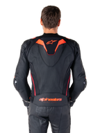 Skórzana kurtka Alpinestars Missile V3 Ignition, widok z tyłu, czarna z akcentami w kolorze fluo czerwonym i ciemnoczerwonym, sportowy garb aerodynamiczny, logo Alpinestars na plecach, noszona z dopasowanymi czarnymi skórzanymi spodniami motocyklowymi, profesjonalna odzież wyścigowa