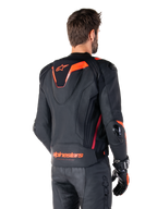 Skórzana kurtka Alpinestars Missile V3 Ignition, męska sportowa kurtka wyścigowa, czarna z akcentami Red Fluo, widok z tyłu prezentujący smukły aerodynamiczny garb i logo Alpinestars na dole pleców, noszona z czarnymi skórzanymi spodniami i rękawicami wyścigowymi, profesjonalny design sportowy
