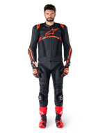 Męski model mający na sobie skórzaną kurtkę Alpinestars Missile V3 Ignition w kolorze Black Red Fluo Dark Red, kompletny motocyklowy strój wyścigowy, w tym pasujące skórzane spodnie, rękawice wyścigowe i buty, z wyraźnym brandingiem Alpinestars na klatce piersiowej, poza przodem, profesjonalny sportowy strój motocyklowy