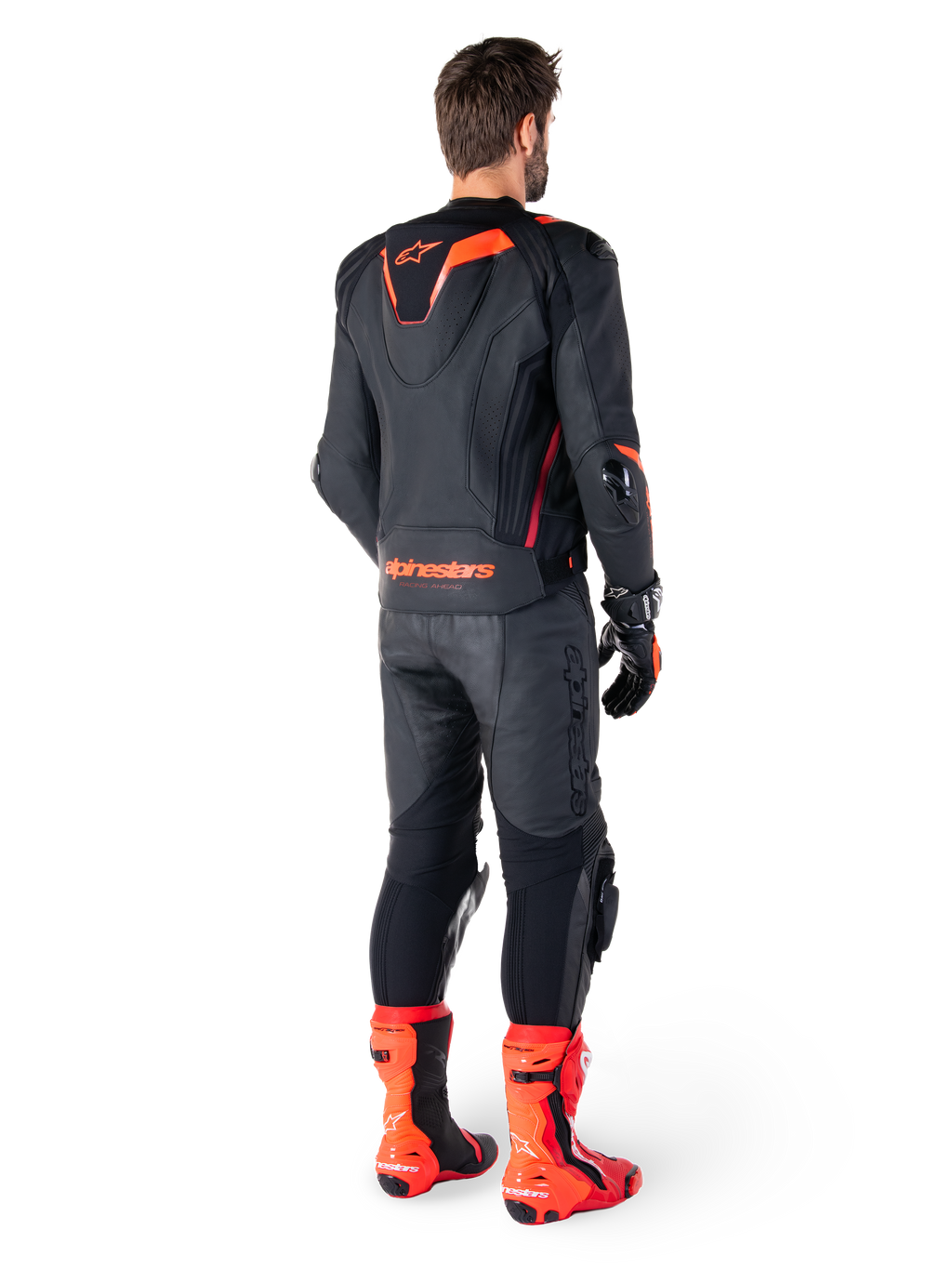 Skórzana kurtka Alpinestars Missile V3 Ignition, sportowa kurtka motocyklowa, czarna i czerwona Fluo, widok z tyłu na motocyklistę ubranego w pełny strój wyścigowy z dopasowanymi skórzanymi spodniami, rękawicami i czerwonymi butami, posiada sportowy garb Aero-hump oraz wyraźne logo w dolnej części pleców.
