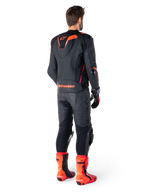 Skórzana kurtka Alpinestars Missile V3 Ignition, sportowa kurtka motocyklowa, czarna i czerwona Fluo, widok z tyłu na motocyklistę ubranego w pełny strój wyścigowy z dopasowanymi skórzanymi spodniami, rękawicami i czerwonymi butami, posiada sportowy garb Aero-hump oraz wyraźne logo w dolnej części pleców.