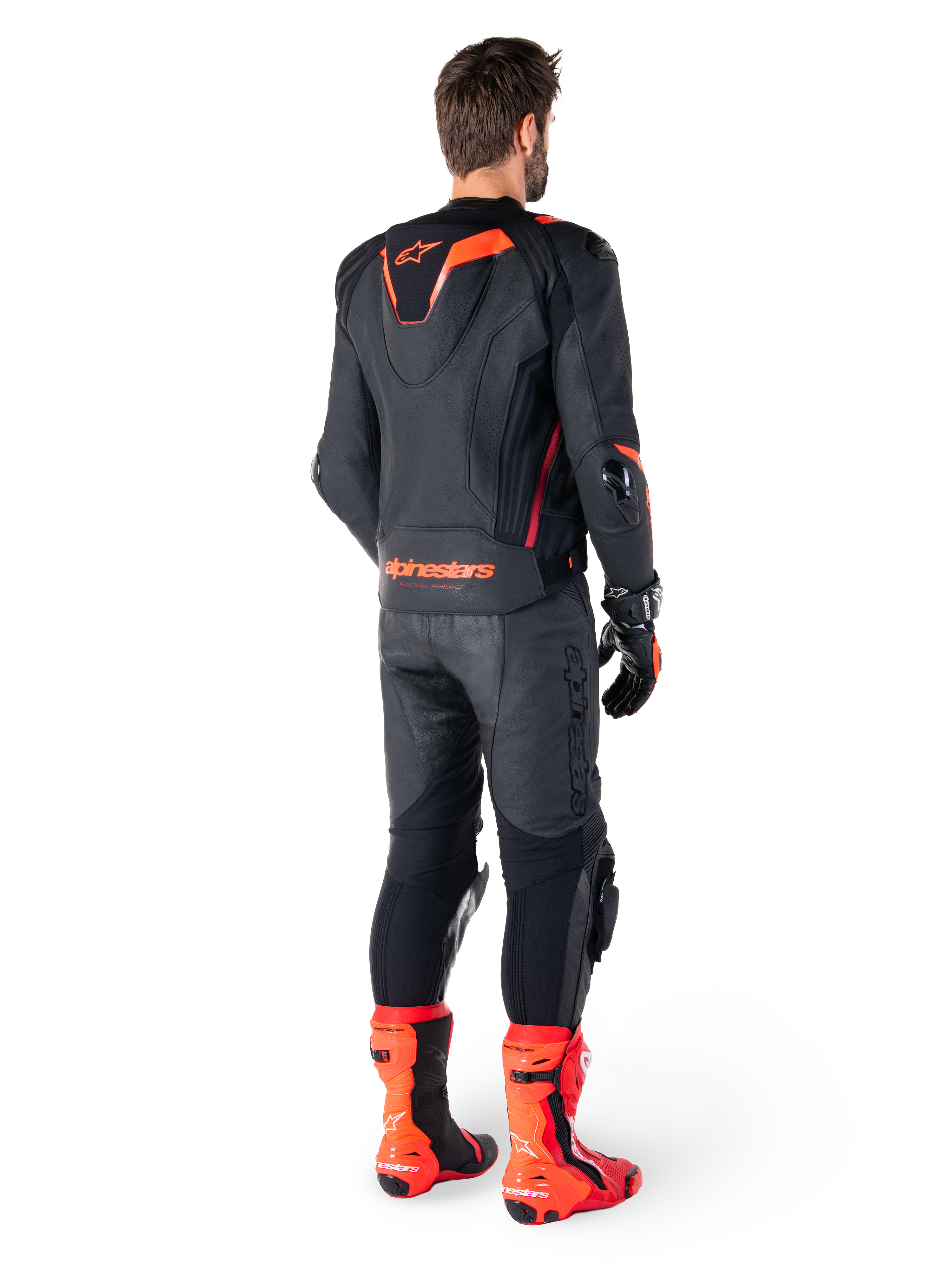 Skórzana kurtka Alpinestars Missile V3 Ignition, sportowa kurtka motocyklowa, czarna i czerwona Fluo, widok z tyłu na motocyklistę ubranego w pełny strój wyścigowy z dopasowanymi skórzanymi spodniami, rękawicami i czerwonymi butami, posiada sportowy garb Aero-hump oraz wyraźne logo w dolnej części pleców.