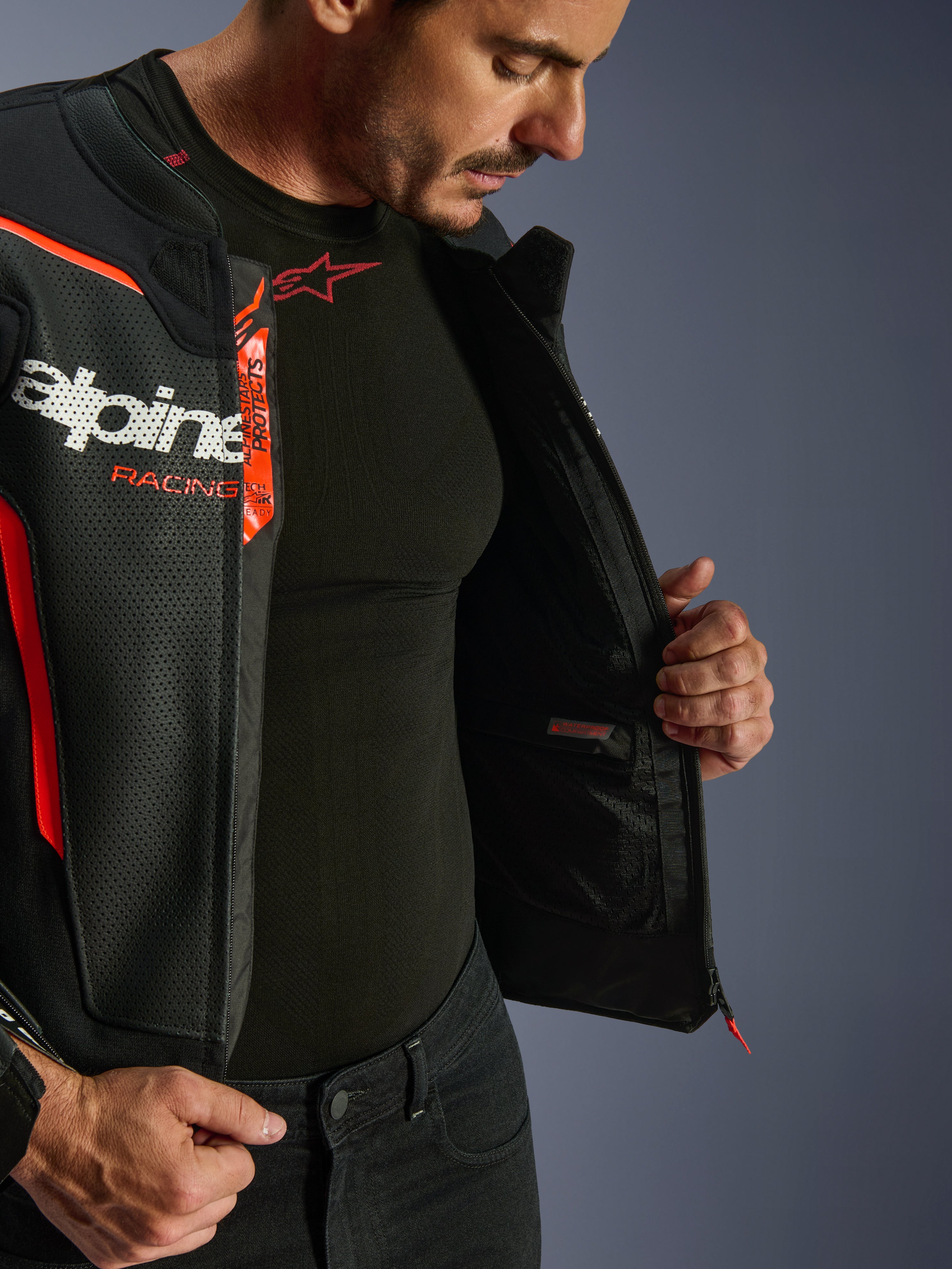 Alpinestars GP Force V2 Air Leather Jacket, czarno-czerwona (Red Fluo), rozpięta, ukazująca wewnętrzną wodoodporną kieszeń i branding, wielopanelowa konstrukcja z perforowanej skóry dla optymalnego przepływu powietrza, noszona z czarną warstwą bazową Alpinestars