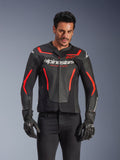 Skórzana kurtka motocyklowa Alpinestars GP Force V2 Air, kurtka wyścigowa, czarna i czerwona fluo, konstrukcja ze skóry premium z licznymi perforacjami zapewniającymi przepływ powietrza, noszona przez modela w czarnych rękawicach i spodniach, z wyraźnym brandingiem i napisem „Racing Ahead” na klatce piersiowej
