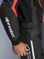 Kurtka skórzana Alpinestars GP Force V2 Air w kolorze czarno-czerwonym (Black Red Fluo), widok szczegółowy z dużym białym logo na rękawie, perforowana skóra zapewniająca przepływ powietrza, noszona z dopasowanymi spodniami motocyklowymi, sportowy design.