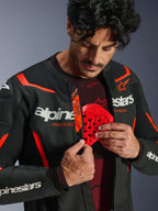 Skórzana kurtka Alpinestars GP Force V2 Air w kolorze czarno-czerwonym (Red Fluo), mężczyzna rozpinający zamek, aby odsłonić wkładany czerwony ochraniacz klatki piersiowej, perforowana skóra, białe logo, oznaczenie Tech-Air Ready na wewnętrznej klapie