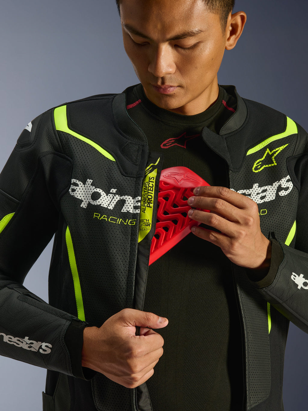 Kurtka skórzana Alpinestars GP Force V2 Air, czarno-żółta fluo, perforowana skórzana kurtka motocyklowa, noszona przez motocyklistę prezentującego komorę na klatkę piersiową z czerwonym wkładem ochronnym, białe logo Alpinestars i rozległe perforacje zapewniające przepływ powietrza.
