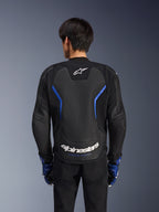 Alpinestars GP Force V2 Airflow Leather Jacket, skórzana kurtka motocyklowa, czarna z metalicznymi niebieskimi akcentami, widok z tyłu, duży perforowany panel na plecach dla wentylacji, białe logo Alpinestars, noszona z niebieskimi rękawicami i czarnymi spodniami do jazdy sportowej
