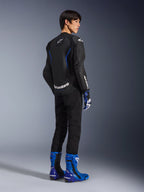 Model widoczny od tyłu w skórzanej kurtce Alpinestars GP Force V2 Airflow w kolorze Black Metallic Blue, z perforowanymi panelami skórzanymi i białymi logo, w zestawieniu z pasującymi rękawicami wyścigowymi i niebieskimi butami, sportowa odzież motocyklowa.