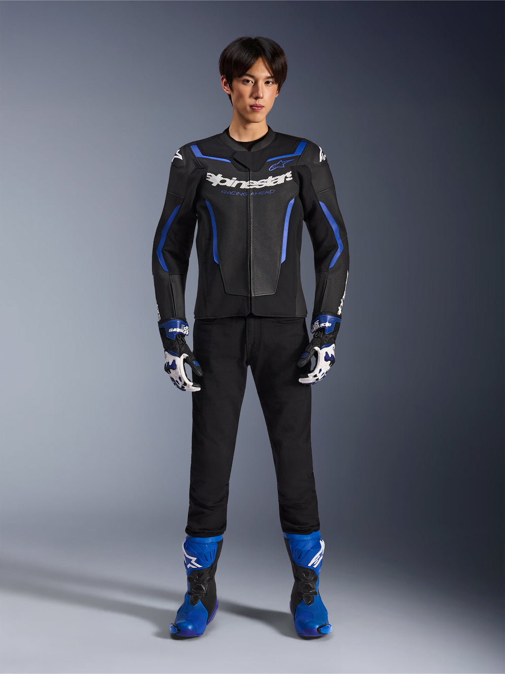 Skórzana kurtka Alpinestars GP Force V2 Airflow w kolorze Black Metallic Blue, noszona z pasującymi rękawicami wyścigowymi, czarnymi spodniami i niebieskimi butami, profesjonalny sportowy zestaw motocyklowy, zdjęcie studyjne całej sylwetki