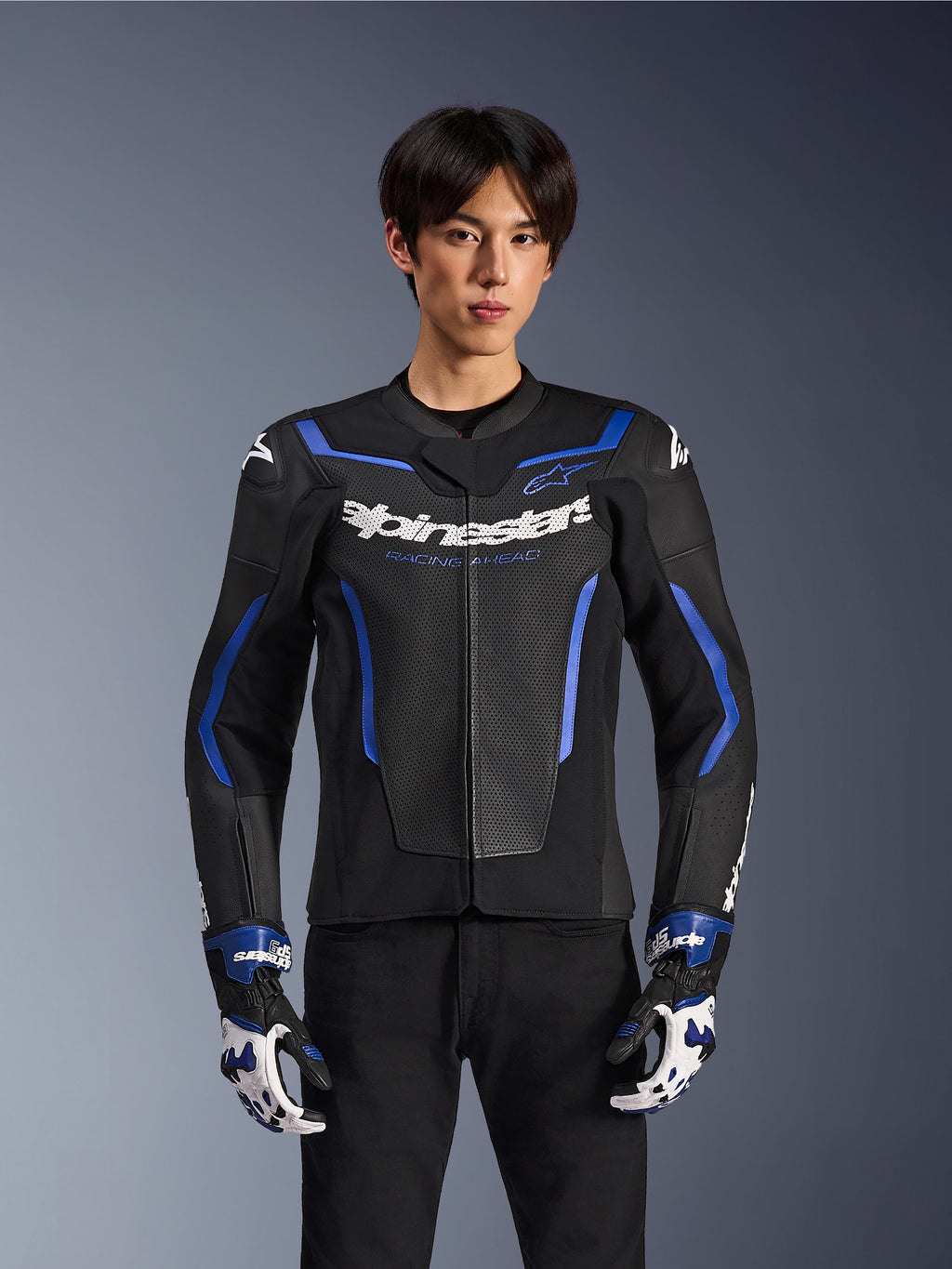 Alpinestars GP Force V2 Airflow Leather Jacket, czarno-niebieska kurtka motocyklowa z perforowanej skóry i niebieskimi akcentami, prezentowana przez modela w pasujących rękawicach wyścigowych i czarnych spodniach, profesjonalna odzież do jazdy sportowej