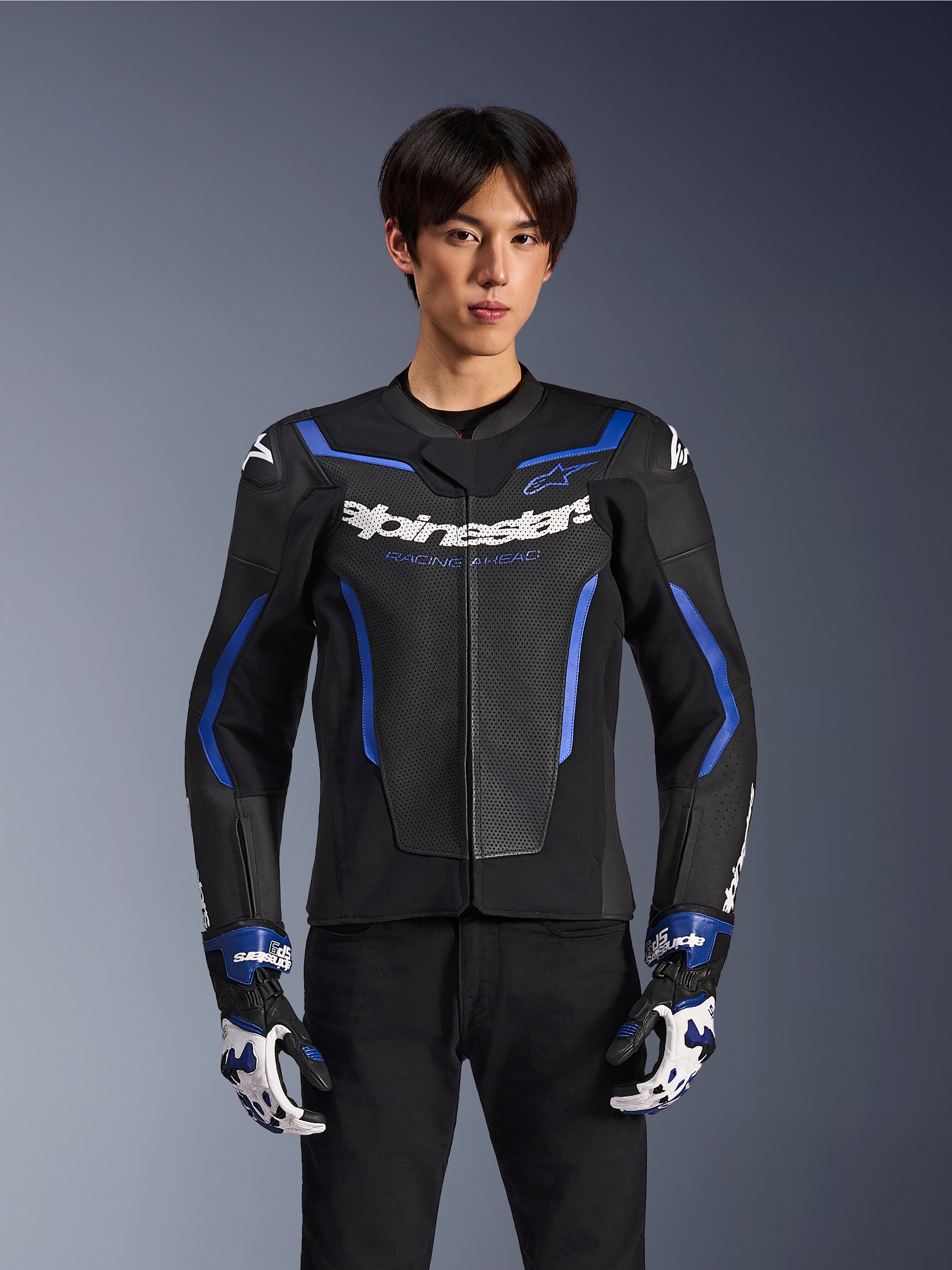 Alpinestars GP Force V2 Airflow Leather Jacket, czarno-niebieska kurtka motocyklowa z perforowanej skóry i niebieskimi akcentami, prezentowana przez modela w pasujących rękawicach wyścigowych i czarnych spodniach, profesjonalna odzież do jazdy sportowej