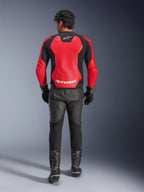 Widok z tyłu motocyklisty w skórzanej kurtce Alpinestars GP Force V2 Air w kolorze czerwono-czarnym, z dużymi perforowanymi panelami i białym logo Alpinestars na plecach, w połączeniu z czarnymi skórzanymi spodniami motocyklowymi i butami wyścigowymi.