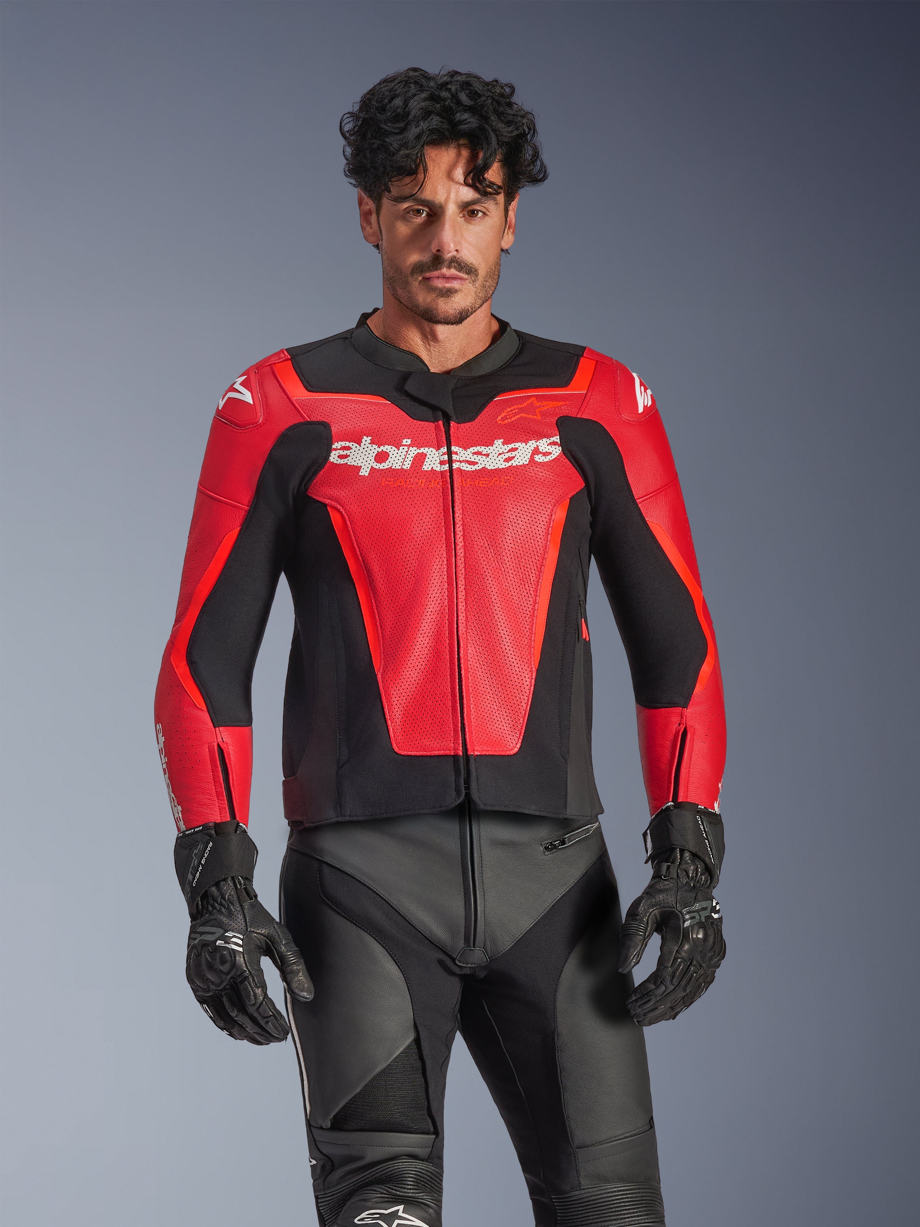 Alpinestars GP Force V2 Air Leather Jacket, czerwono-czarna motocyklowa kurtka wyścigowa, konstrukcja z perforowanej skóry z białym logo Alpinestars, noszona przez modela w zestawieniu z czarnymi spodniami wyścigowymi i rękawicami