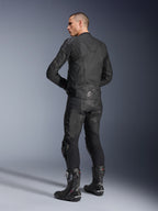 Alpinestars Dusk Leather Jacket, czarna skórzana kurtka motocyklowa, widok z tyłu pod kątem trzech czwartych na modelu ubranym w pasujące skórzane spodnie i wyczynowe buty wyścigowe, posiada elastyczne panele harmonijkowe, srebrne logo gwiazdy na dole pleców i branding DUSK w górnej części, profesjonalne zdjęcie studyjne