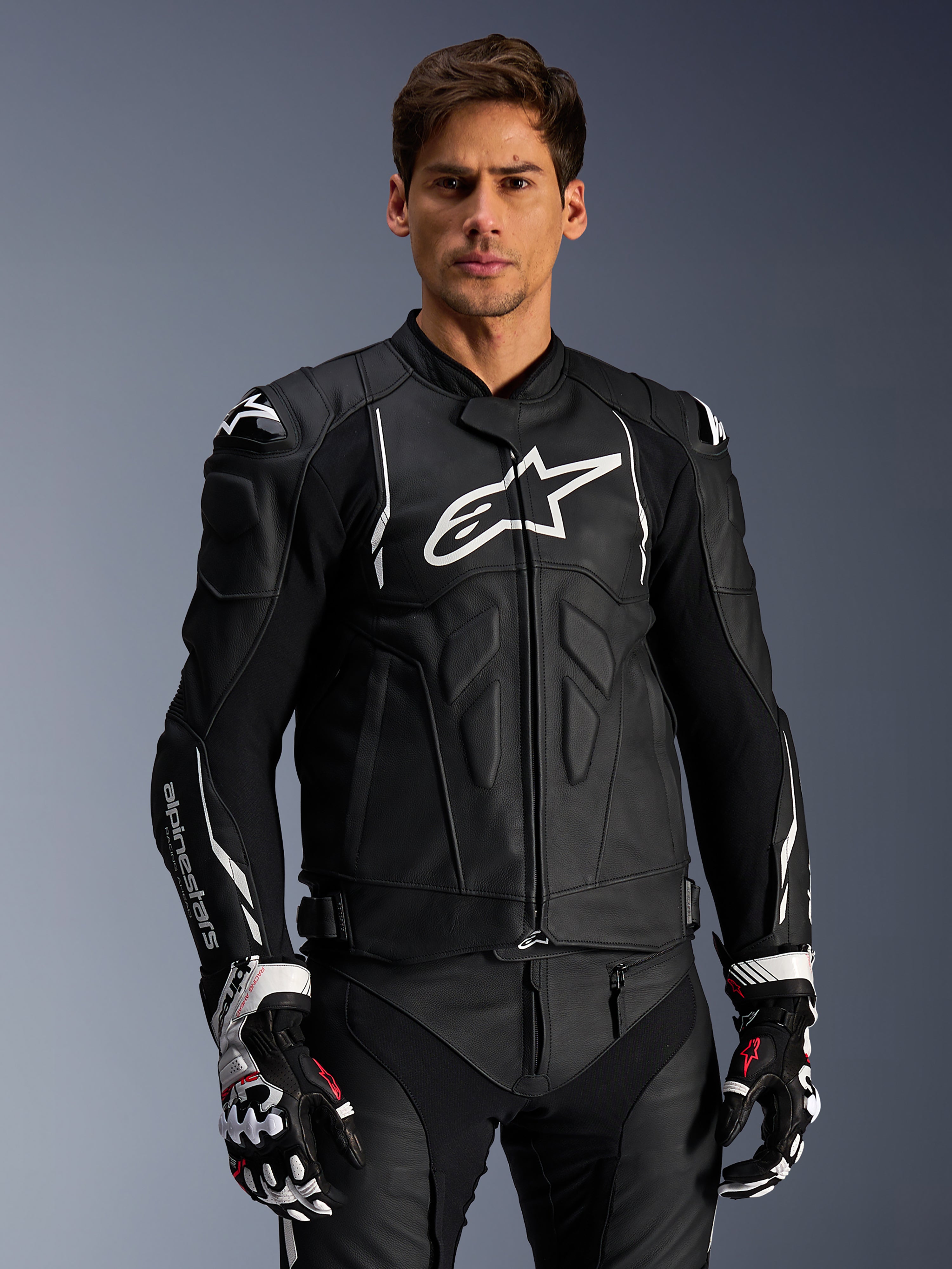 Alpinestars Dusk Leather Jacket, czarno-biała skórzana kurtka motocyklowa z wyściełanymi strefami ochronnymi i białymi logo, zestawiona z czarno-białymi rękawicami wyścigowymi z czerwonymi akcentami, profesjonalna sportowa odzież motocyklowa