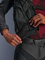 Alpinestars Dusk Leather Jacket, czarna, zbliżenie na zamek łączący w pasie przypinany do skórzanych spodni motocyklowych, noszona z czerwono-czarną wzorzystą warstwą bazową, wytrzymała skórzana konstrukcja do jazdy szosowej