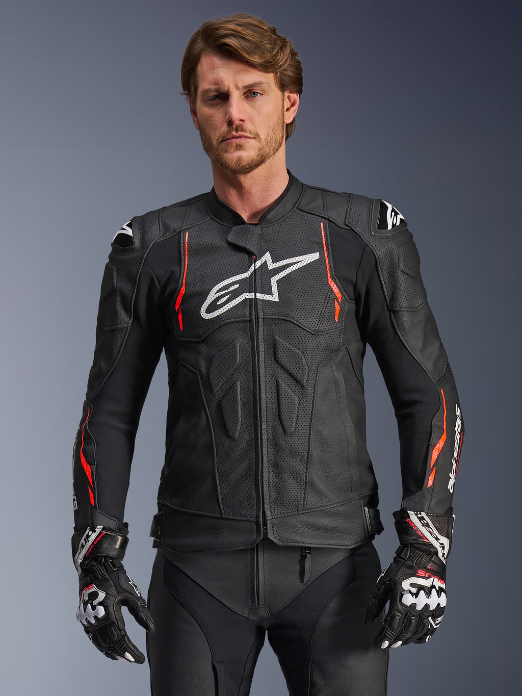 Alpinestars Dusk Airflow Leather Jacket, czarna z akcentami Red Fluo i białymi, skórzana kurtka motocyklowa wyścigowa, rozległe perforacje dla wentylacji, białe logo na piersi i zewnętrzne slidery na ramionach, prezentowana przez modela z dopasowanymi rękawicami wyścigowymi