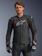 Alpinestars Dusk Airflow Leather Jacket, czarna z akcentami Red Fluo i białymi, skórzana kurtka motocyklowa wyścigowa, rozległe perforacje dla wentylacji, białe logo na piersi i zewnętrzne slidery na ramionach, prezentowana przez modela z dopasowanymi rękawicami wyścigowymi