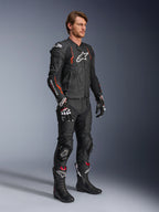 Skórzana kurtka Alpinestars Dusk Airflow, Black Red Fluo, noszona jako część kompletnego motocyklowego stroju wyścigowego z dopasowanymi skórzanymi spodniami, rękawicami i butami, charakteryzująca się perforowaną skórzaną konstrukcją i sportowymi akcentami.