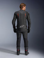 Skórzana kurtka Alpinestars Dusk Airflow, czarna i czerwona fluo, widok z tyłu ukazujący rozległe perforacje i duże białe logo w dolnej części pleców, noszona z pasującym skórzanym strojem wyścigowym, w tym spodniami, butami i rękawicami