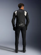 Alpinestars Dusk Airflow Leather Jacket, czarno-biała, widok z tyłu motocyklisty w czarnych spodniach i butach, z perforowaną skórą dla wentylacji, białymi elastycznymi panelami akordeonowymi na ramionach i białym logo w dolnej części pleców