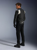 Alpinestars Dusk Airflow Leather Jacket, czarno-biała, widok z tyłu na modela ubranego w perforowaną kurtkę skórzaną z dopasowanymi czarnymi spodniami i butami, białe akordeonowe panele elastyczne i wyraźne logo w dolnej części pleców, sportowy strój motocyklowy