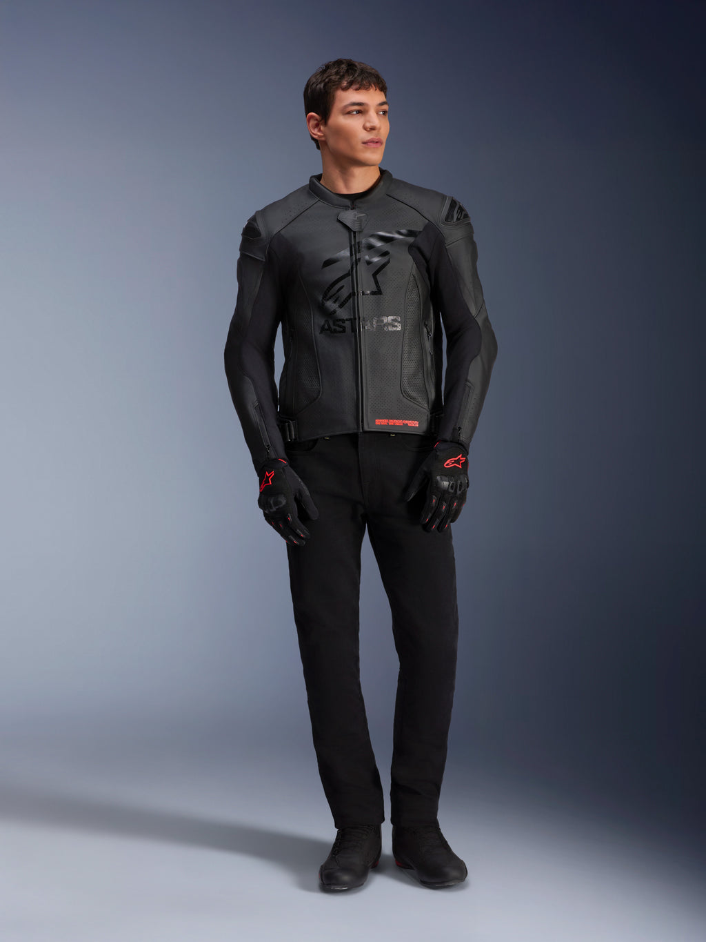 Skórzana kurtka Alpinestars GP Plus R V4 Airflow, czarna, noszona przez modela z pasującymi czarnymi rękawicami i spodniami, z perforowanymi panelami skórzanymi, dużym stonowanym logo z gwiazdą na klatce piersiowej i dopasowanym sportowym krojem