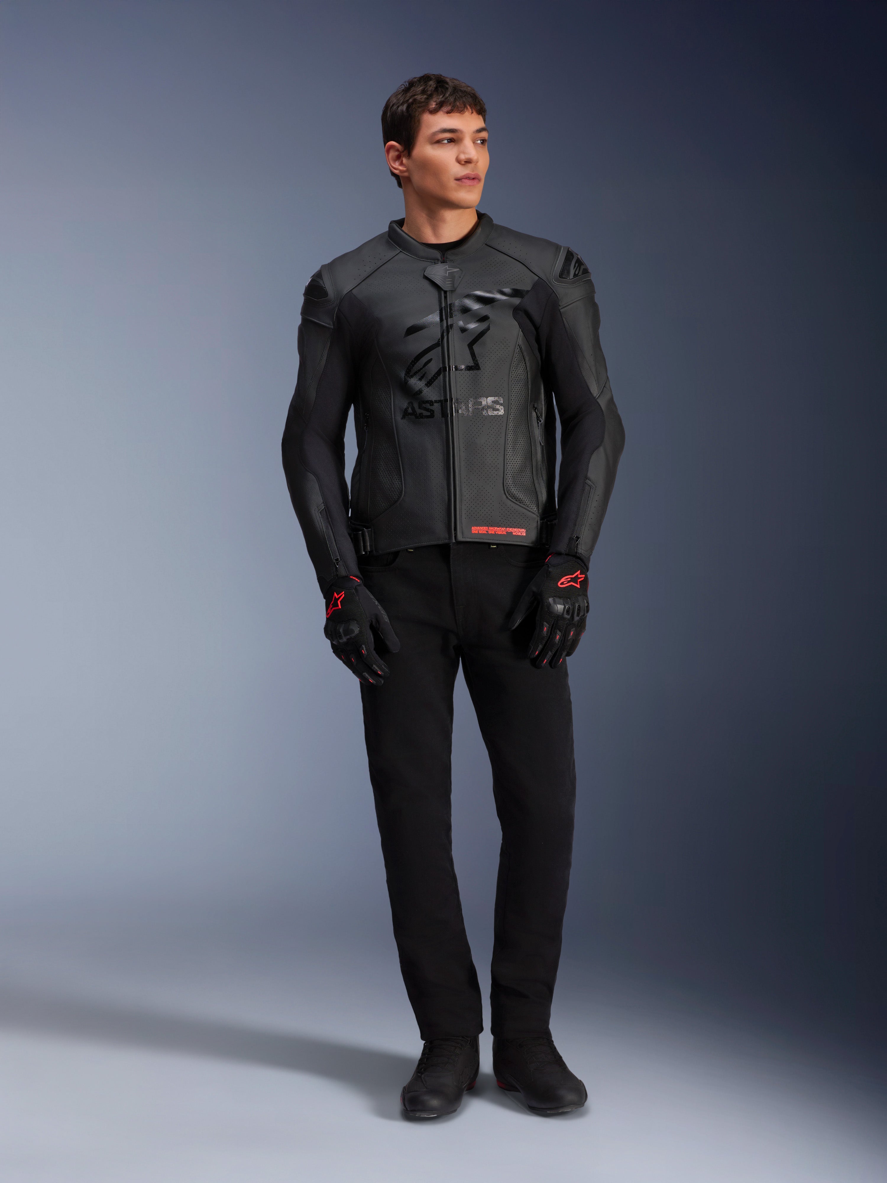 Skórzana kurtka Alpinestars GP Plus R V4 Airflow, czarna, noszona przez modela z pasującymi czarnymi rękawicami i spodniami, z perforowanymi panelami skórzanymi, dużym stonowanym logo z gwiazdą na klatce piersiowej i dopasowanym sportowym krojem