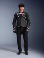 Model w skórzanej kurtce Alpinestars Atem V5 w kolorze czarno-białym, z białym brandingiem Alpinestars i czerwonym logo gwiazdy na piersi, w zestawieniu z czarnymi spodniami i czarno-białymi rękawicami wyścigowymi, profesjonalna odzież motocyklowa