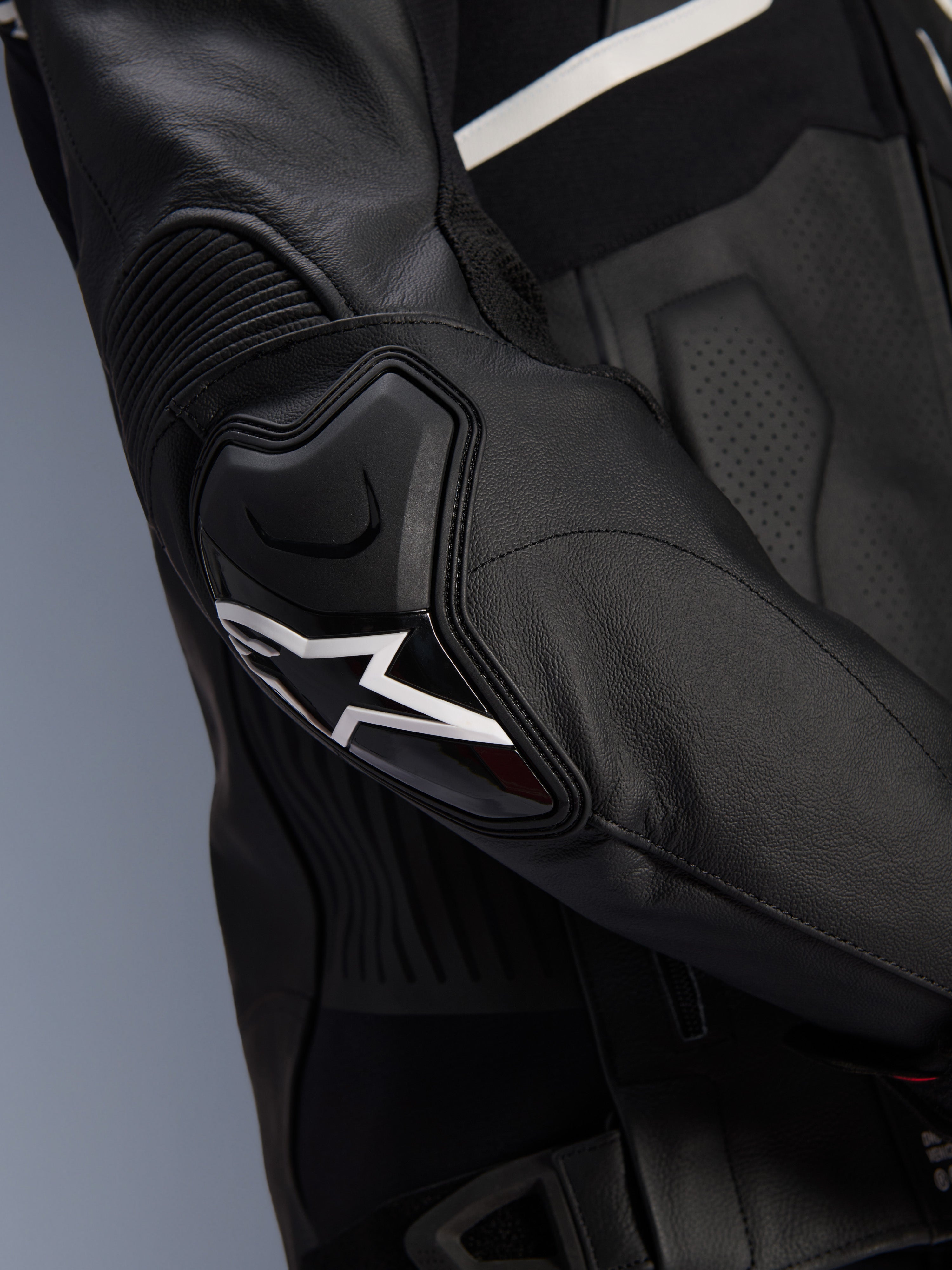 Alpinestars Atem V5 Leather Jacket, czarno-biała, zbliżenie na ochraniacz łokcia DFS RR z białym logo gwiazdy, skórzane panele akordeonowe i perforowana tekstura do jazdy sportowej