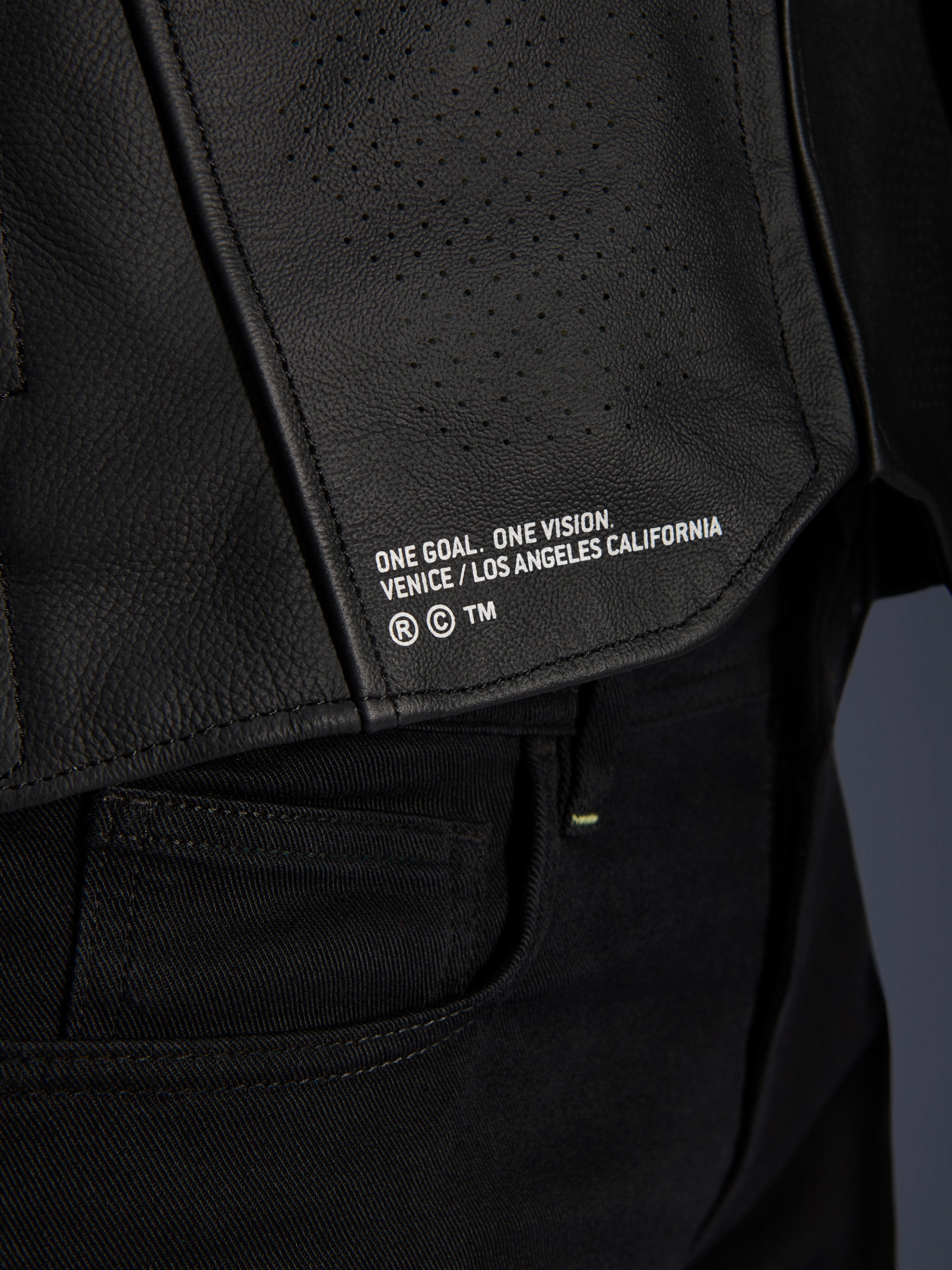 Skórzana kurtka Alpinestars Atem V5, czarna, zbliżenie na dolny tylny panel z napisem „ONE GOAL. ONE VISION. VENICE / LOS ANGELES CALIFORNIA”, widoczna tekstura perforowanej skóry