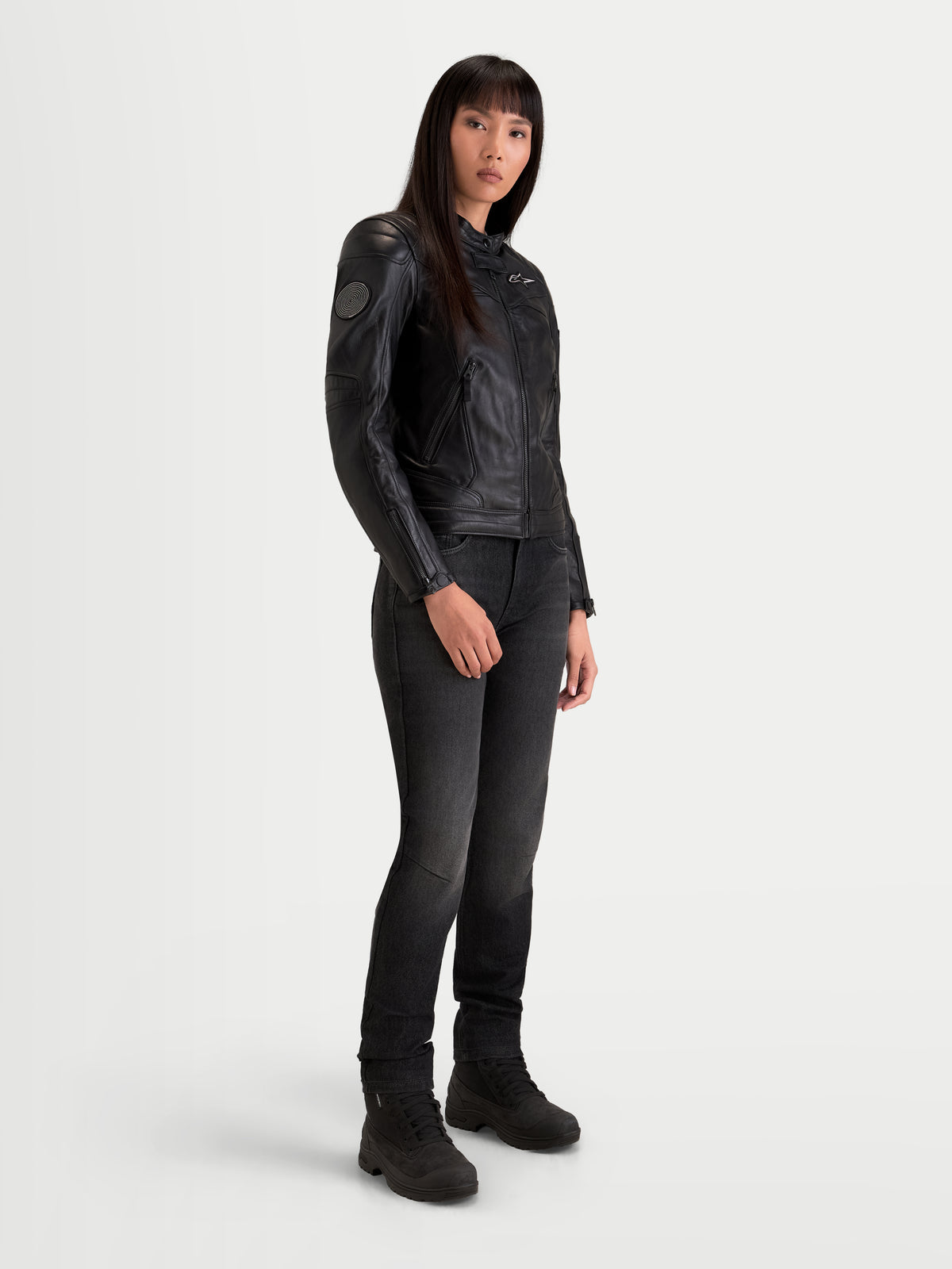 Alpinestars Revea Women Leather Jacket, damska miejska kurtka motocyklowa w kolorze czarnym, widok z trzy czwarte na modelkę w ciemnych jeansach i botkach motocyklowych, konstrukcja z licowej skóry bydlęcej o klasie bezpieczeństwa AA