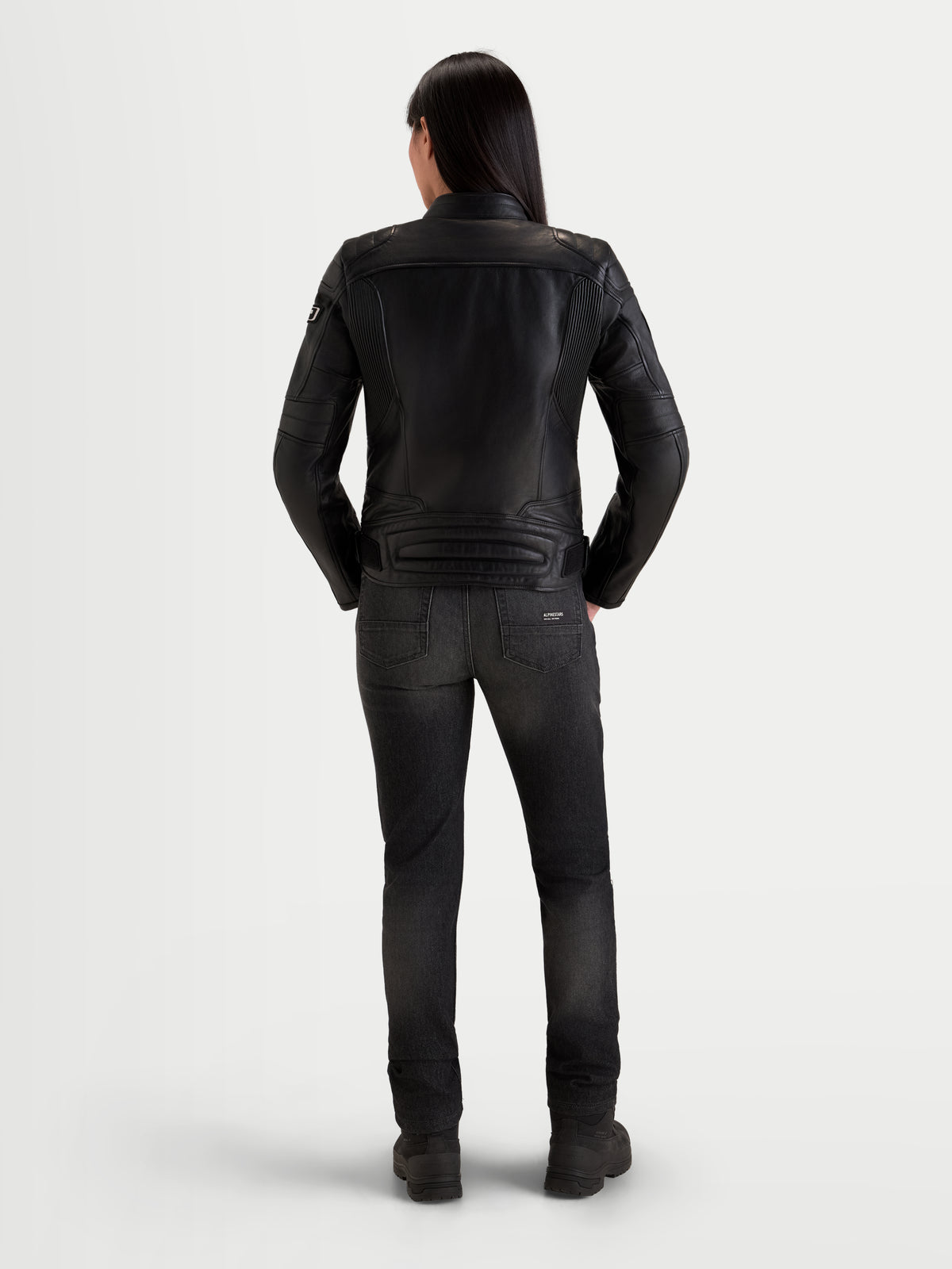 Alpinestars Revea Kurtka skórzana damska, czarna kurtka motocyklowa miejska, widok z tyłu na modelkę w ciemnych jeansach i botkach motocyklowych, konstrukcja z najwyższej jakości skóry bydlęcej