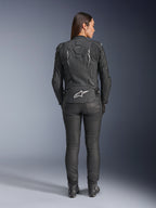 Damska skórzana kurtka Alpinestars Stella Dusk, czarna, widok z tyłu z białym logo Alpinestars na dole pleców i brandingiem „DUSK” w górnej części pleców, noszona z czarnymi spodniami motocyklowymi i butami, prezentująca dopasowany damski krój oraz ochronną skórzaną konstrukcję.