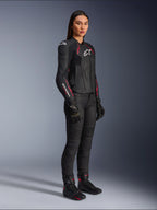 Damska kurtka skórzana Alpinestars Stella Dusk, czarna z różowymi (Diva Pink) i białymi akcentami, prezentowana przez modelkę w czarnych spodniach i butach motocyklowych, gładka skórzana konstrukcja z różowymi detalami i białym logo