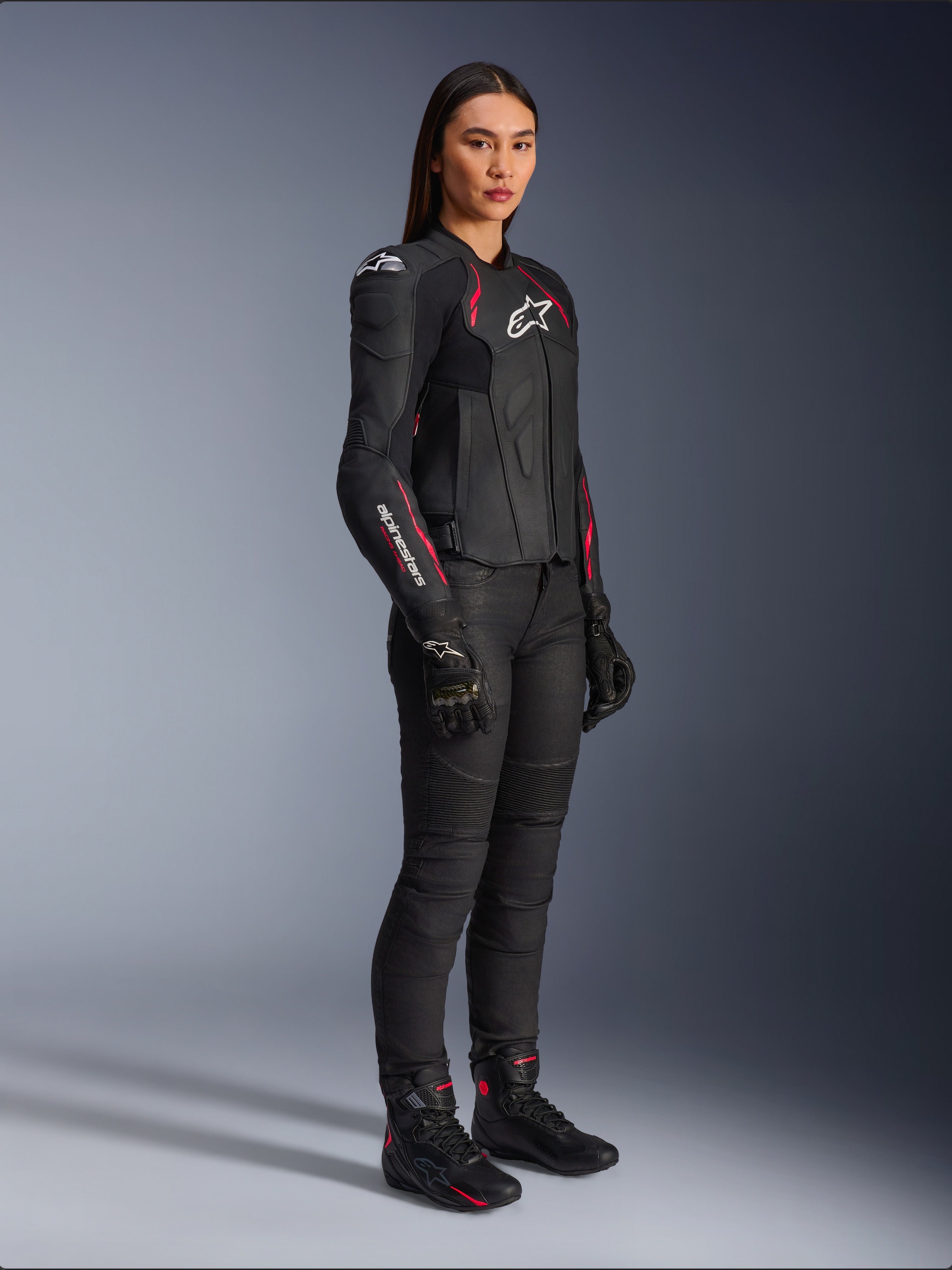 Damska kurtka skórzana Alpinestars Stella Dusk, czarna z różowymi (Diva Pink) i białymi akcentami, prezentowana przez modelkę w czarnych spodniach i butach motocyklowych, gładka skórzana konstrukcja z różowymi detalami i białym logo